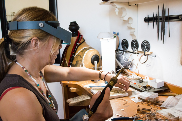 A woman wearing safety equipment on her head as she solders jewelry