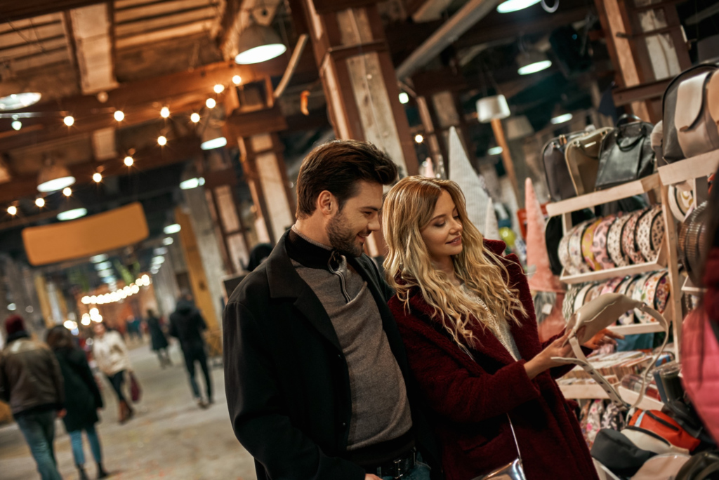 Happy young couple choosing handmade bags at small street market